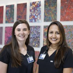 2 smiling APP fellows: both women with long hair in dark shirts with nametags