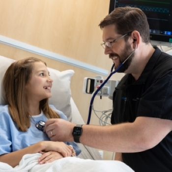 male healthcare worker in blue scrubs caring for girl patient in hospital room