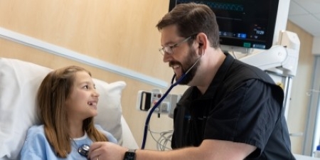 male healthcare worker in black scrubs caring for girl patient in hospital room