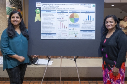 2 women stand on each side of research poster on easel