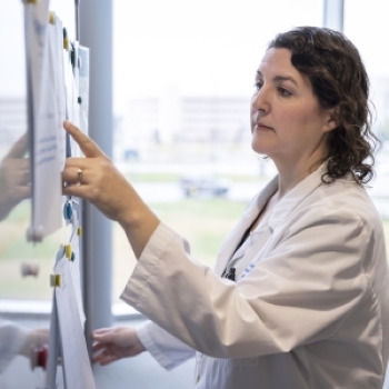 woman in white jacket points to notes on whiteboard