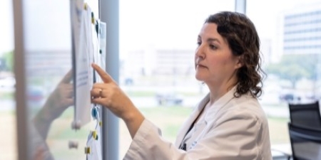 woman in white jacket points to notes on whiteboard