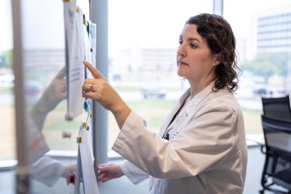 woman in white jacket points to notes on whiteboard