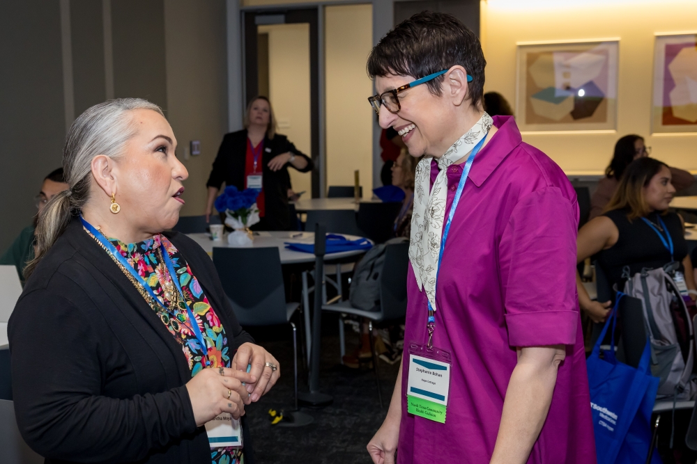 2 women stand talking in conference area