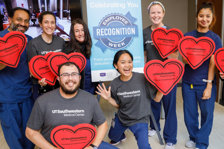 Employees pose with red heart-shaped awards around a banner that says Employee Recognition Week