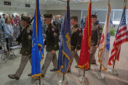 group of men in miltary uniforms marching beside various flags