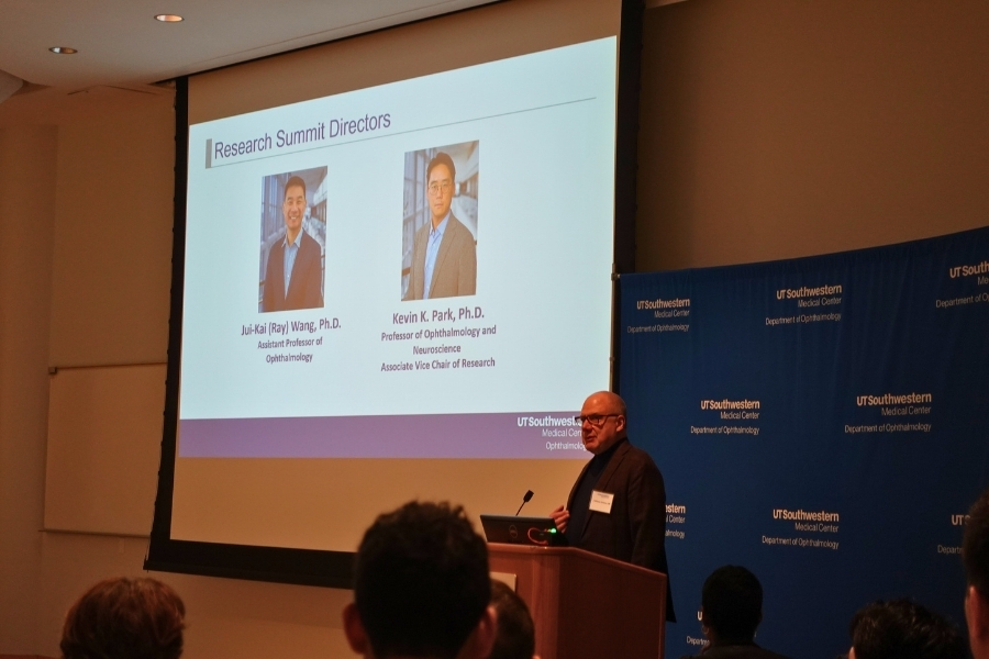 Man standing at a podium next to a slide displaying the conference's event directors, Ray Wang, Ph.D., and Kevin Park, Ph.D.