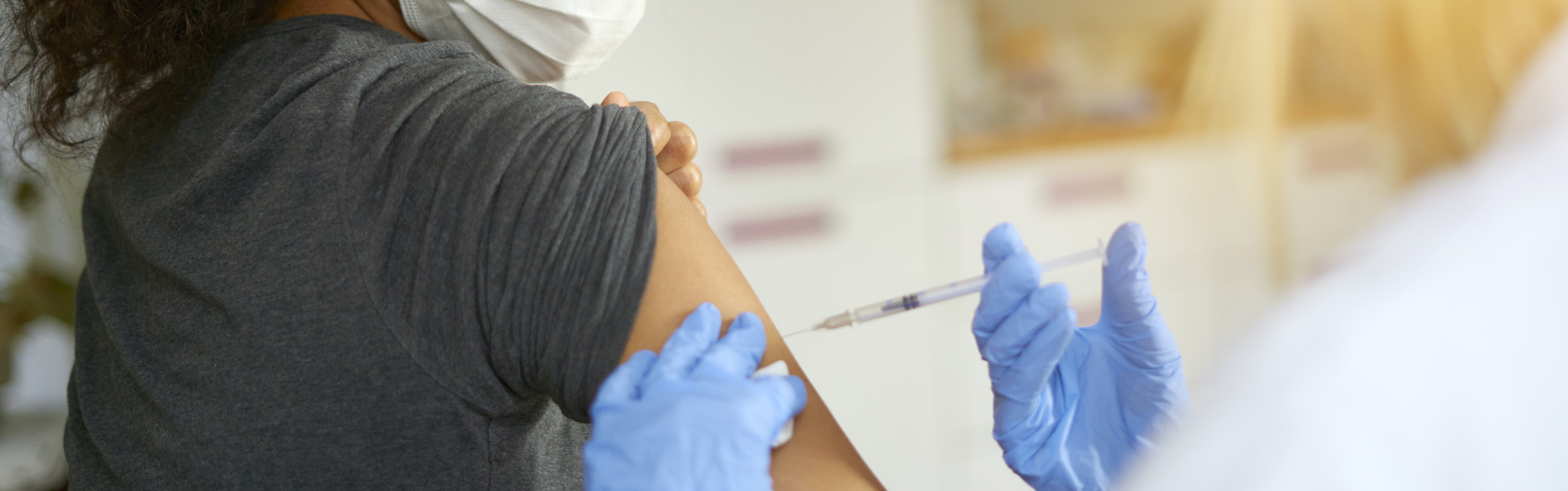 Masked patient receiving an injection from a gloved provider.
