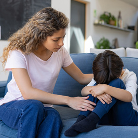 Photo of a woman comforting a sad child with his head on his knees