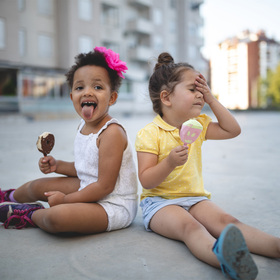 Photo of two children eating ice cream. One of them is holding her head as if it hurts