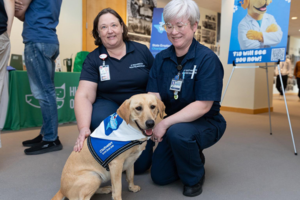 Two women pose with yellow lab, Tia