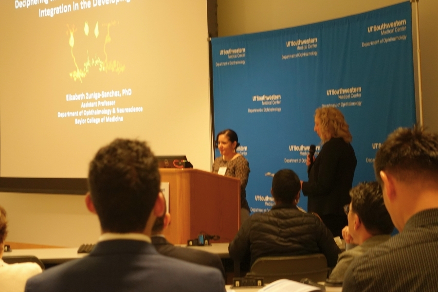 Woman at a podium getting ready to present as a woman with a microphone introduces her