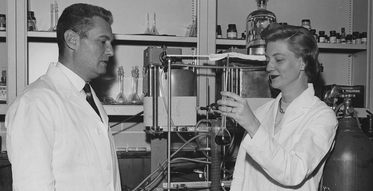 Man and woman in lab coats looking at the content of a beeker.