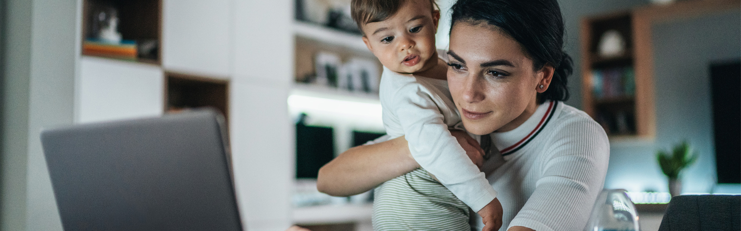 Young modern mother with a baby trying to work on laptop at home and looking tired