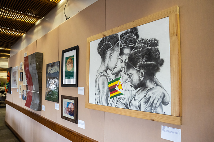 gallery wall of 8 art pieces in various sizes; far left is large multimedia piece containing 3 little girls and a flag
