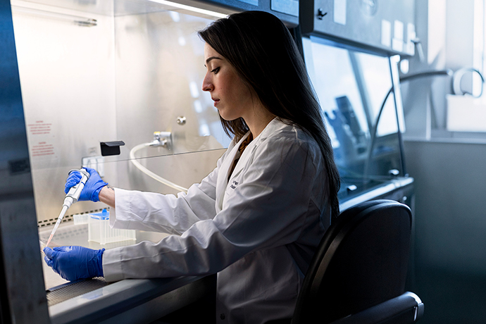Woman at a desk, in a lab, using a dropper.