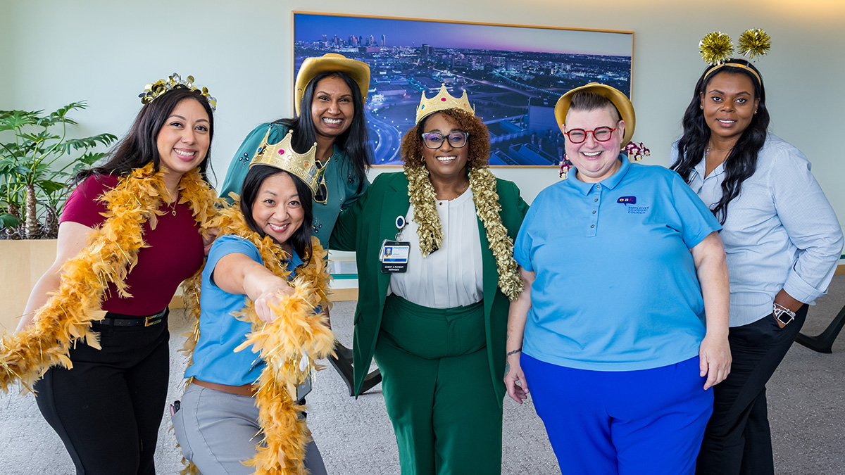Six employees pose with boas, crowns, and silly hats.