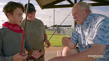 Older man talks to two boys at a baseball diamond.