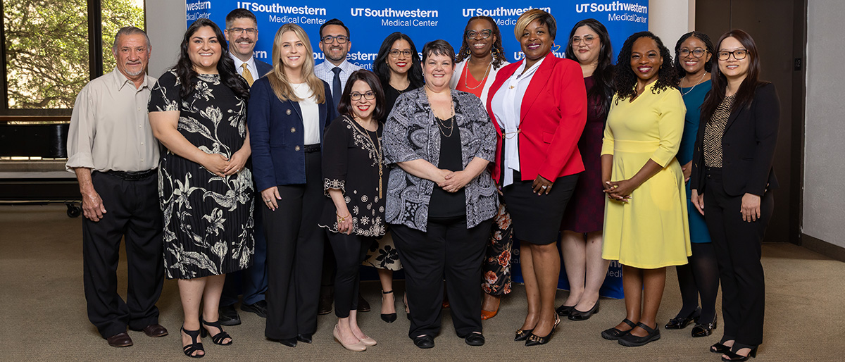 diverse group of 14 employees stand in front of blue UTSW backdrop