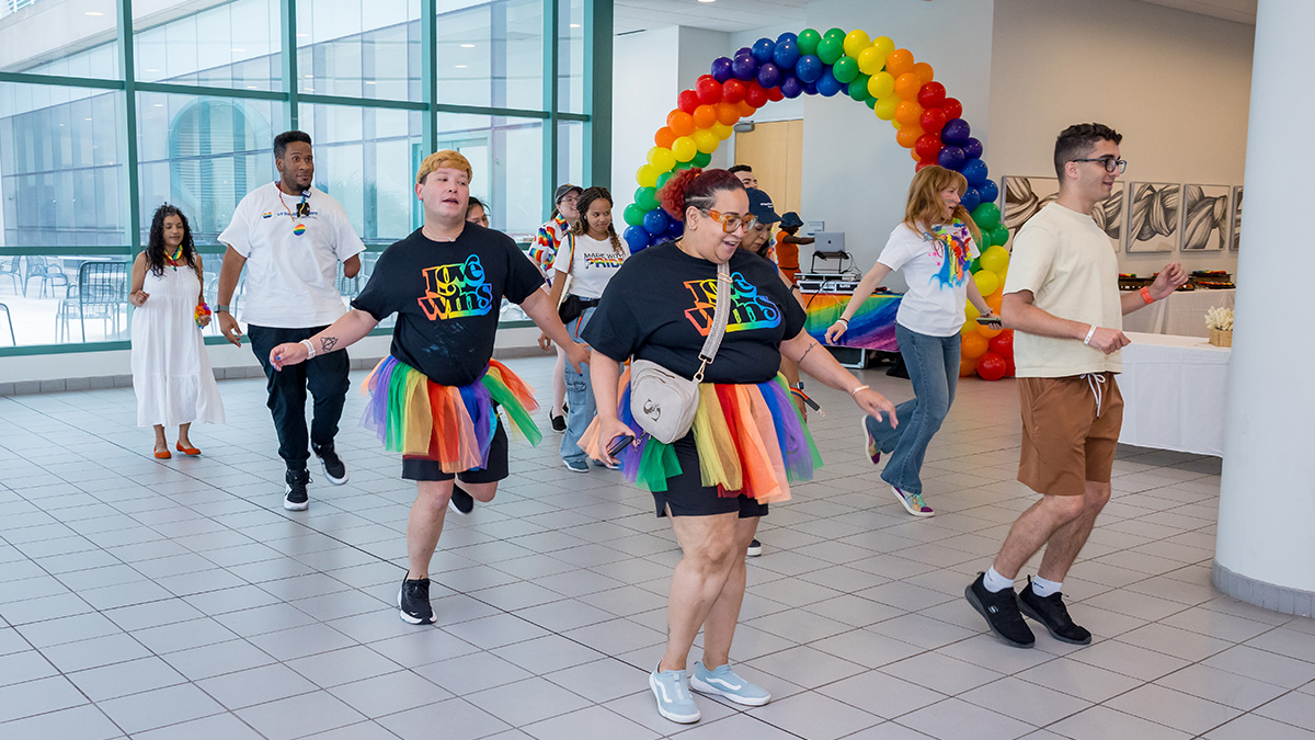 Participants line dancing in front of a rainbow arch of balloons.