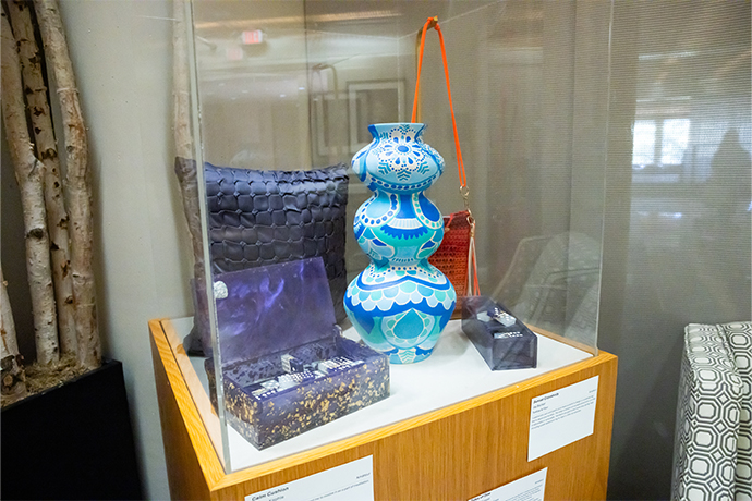 glass case on wood base displays 2 cushions, ornate boxes and blue patterned vase