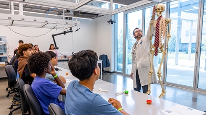 bearded man in lab coat points out a model skeleton for a class of young students