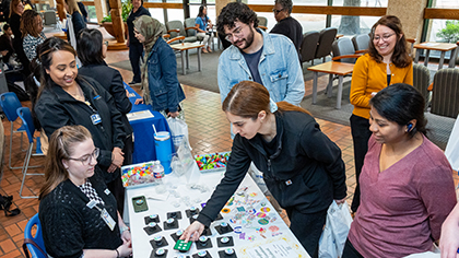 Men and women gather to look at small items displayed on a table.