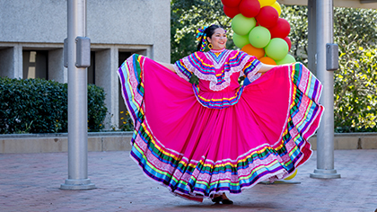 A woman in a colorful costume dances on the plaza cobblestones.