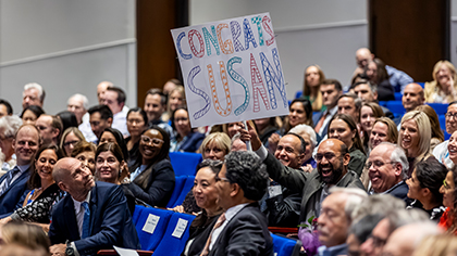 Man in audience holds a sign that reads, Congrats Susan