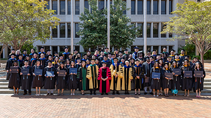 Crowd of students and faculty in cap and gown gather outside building on UTSW campus.