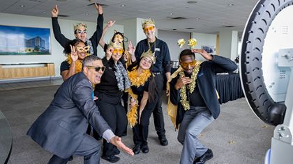 8 happy UTSW employees pose for the selfie-cam wearing sunglasses, gold boas, paper crowns