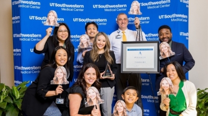 group of diverse UTSW employees pose in front of blue UTSW backdrop holding cutout pictures of woman