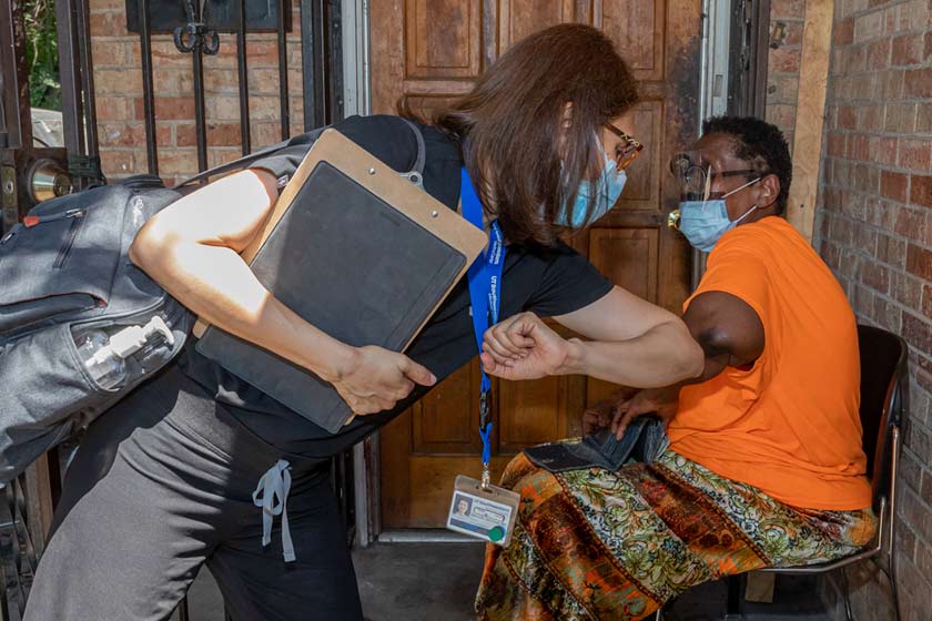 Visitor bumps elbows with an elderly patient on patients front porch.