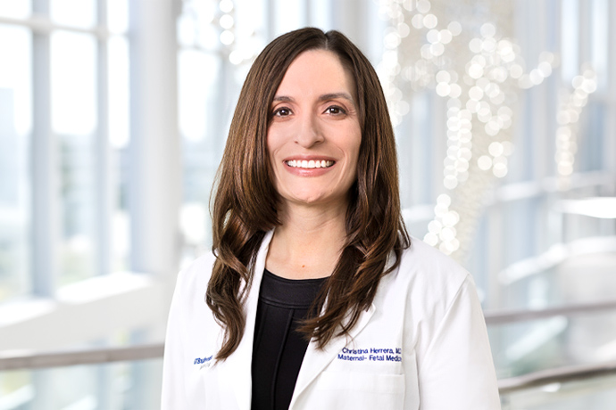 Smiling woman with long dark hair, wearing a lab coat with the UTSW logo.