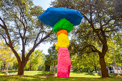 Colorful stones stacked to resemble a tree, standing in a grove of live trees.