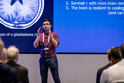 dark haired man on stage presenting in front of blue projection screen