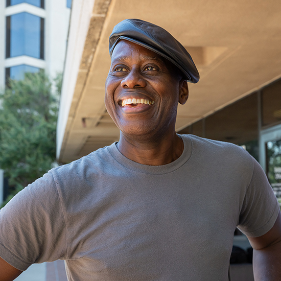 Smiling man wearing a gray tshirt and cap.