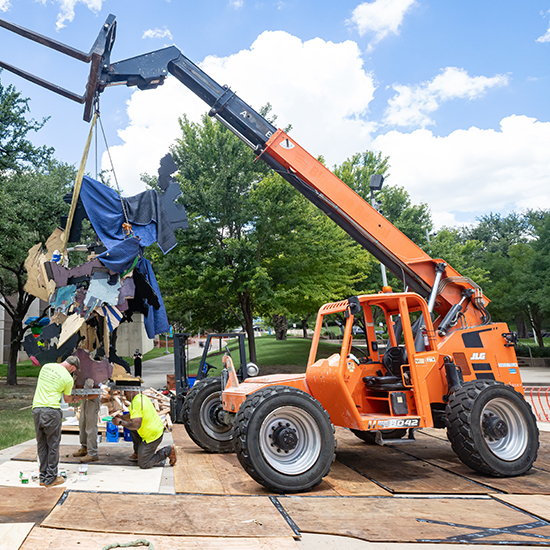 Small orange crane lifting a sculpture into place.