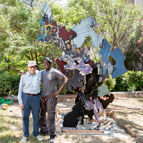 Two smiling men standing next to an assembled piece of sculpture.
