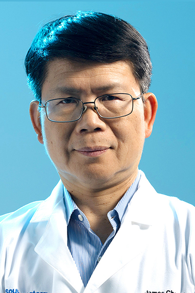 Man with thick dark hair, wearing a white UT Southwestern lab coat over a blue shirt and glasses.