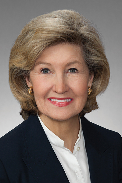 Smiling woman with blond hair, wearing a black jacket over a white blouse.