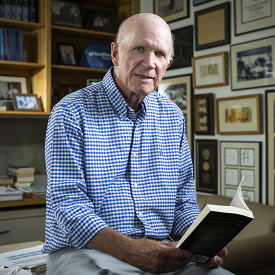 Man leans against desk holding an open book.