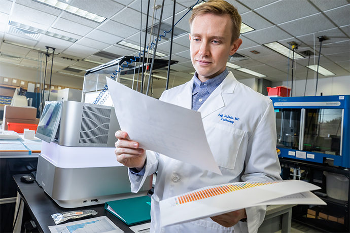 blonde man in white coat looks over papers with equipment in background