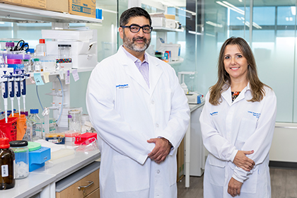in lab, bearded man with glasses stands at left of woman with long dark blonde hair