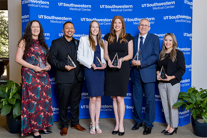 Six men and women hold their glass Pinnacle awards.