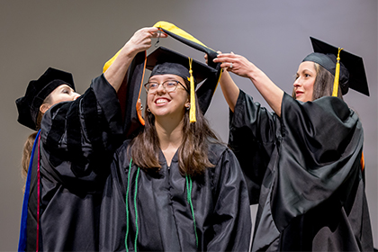smiling girl with glasses in cap and gown receives gold sash