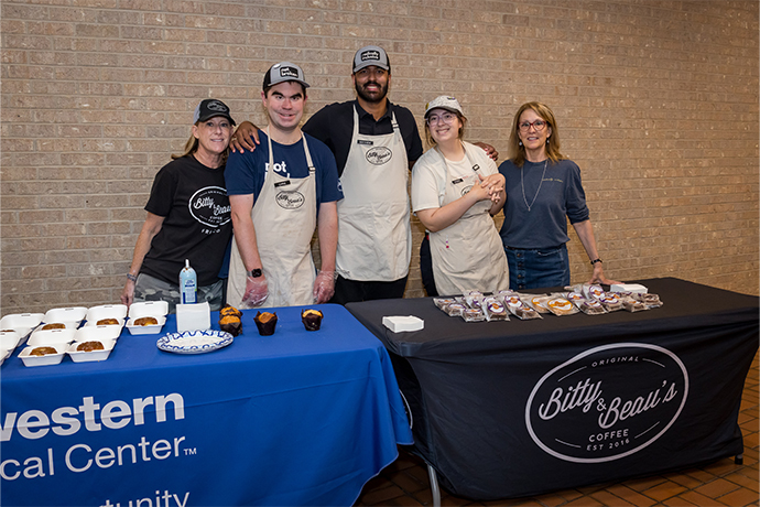 Five people pose behind a table labeled Original Bitty & Beau's Coffee est 2016, covered with treats.