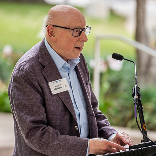 Man speaking at a UTSW podium - Joseph L Goldstein, M.D.