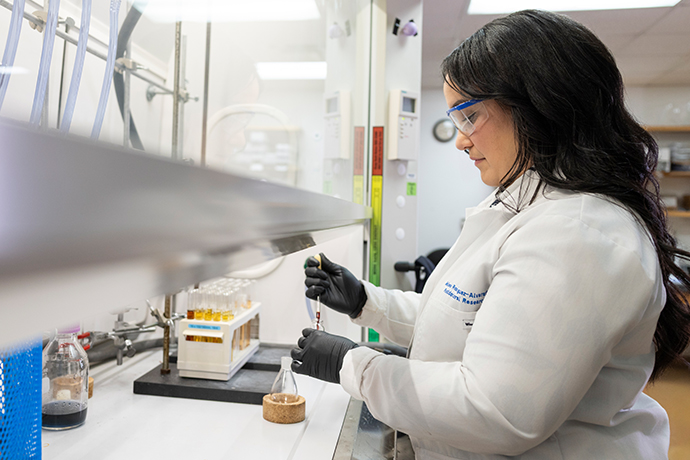 woman with long dark hair in white lab coat does experiment with pipette in lab
