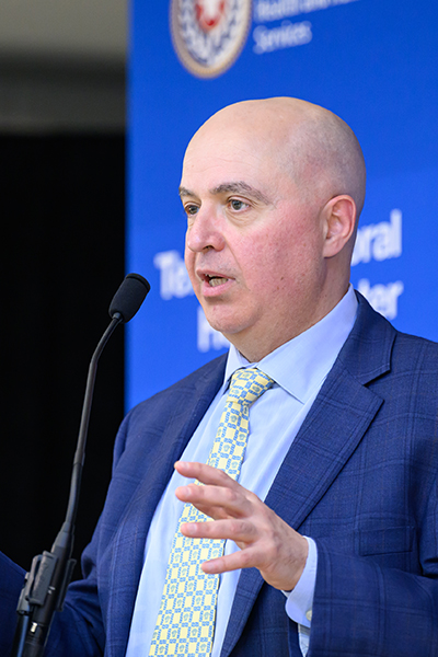 Man wearing suit speaks from podium.